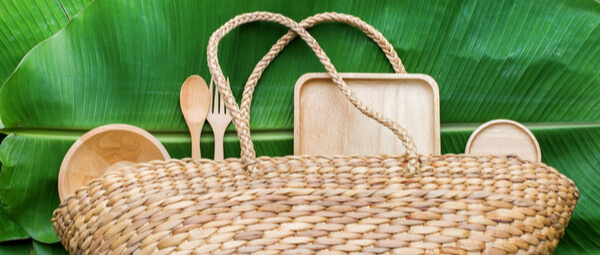 Wicker picnic bag with cutlery, plates, dishes and boards on palm leafs